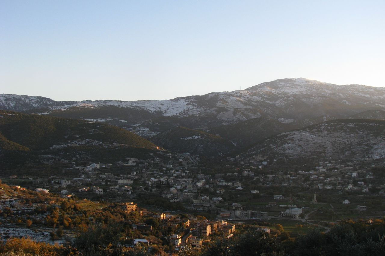 Kobayat spread across the hillsides in late-afternoon sun, below a snow-dusted mountain ridge