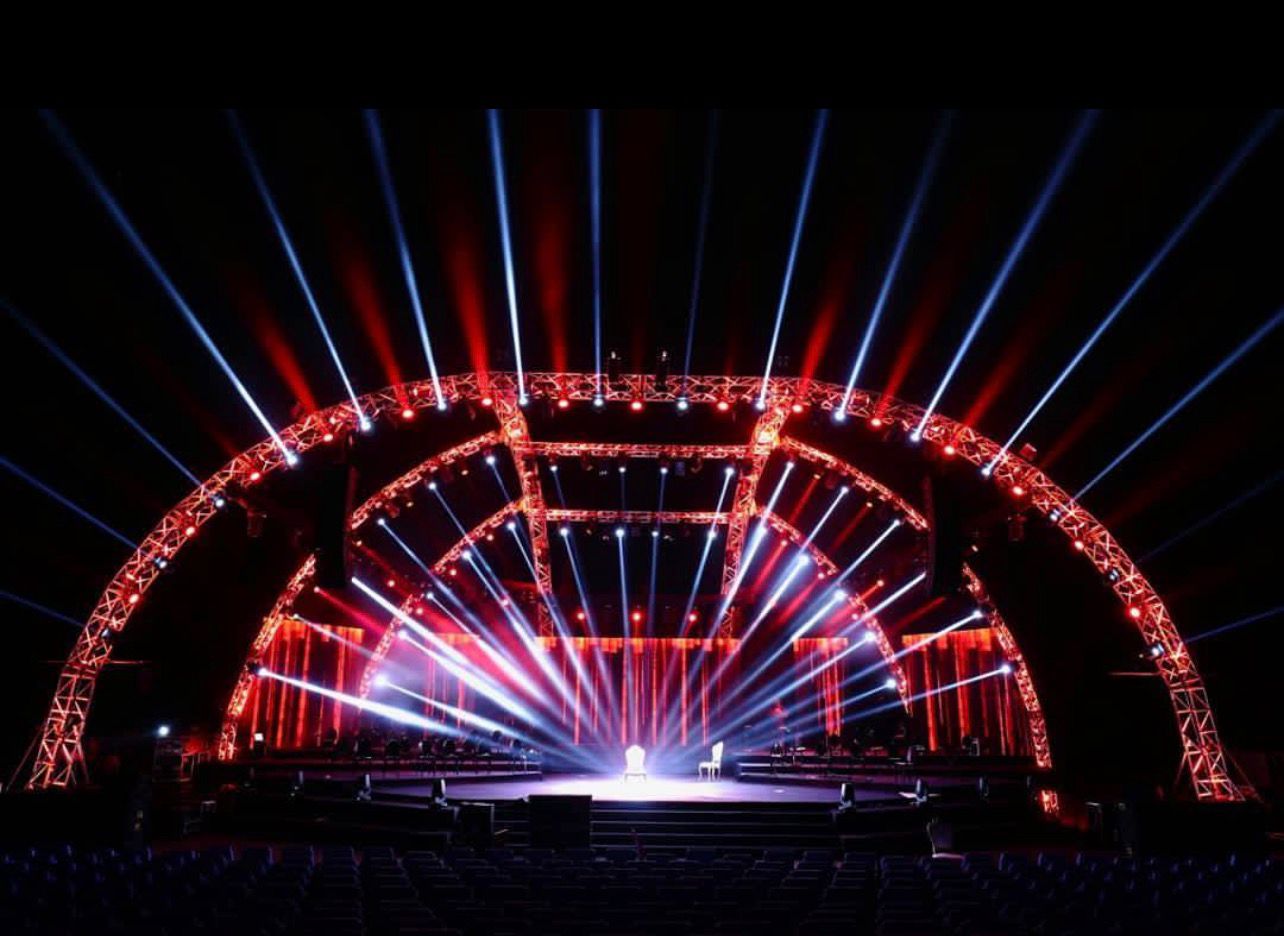 Large outdoor concert stage with dramatic red and blue lighting beams at night