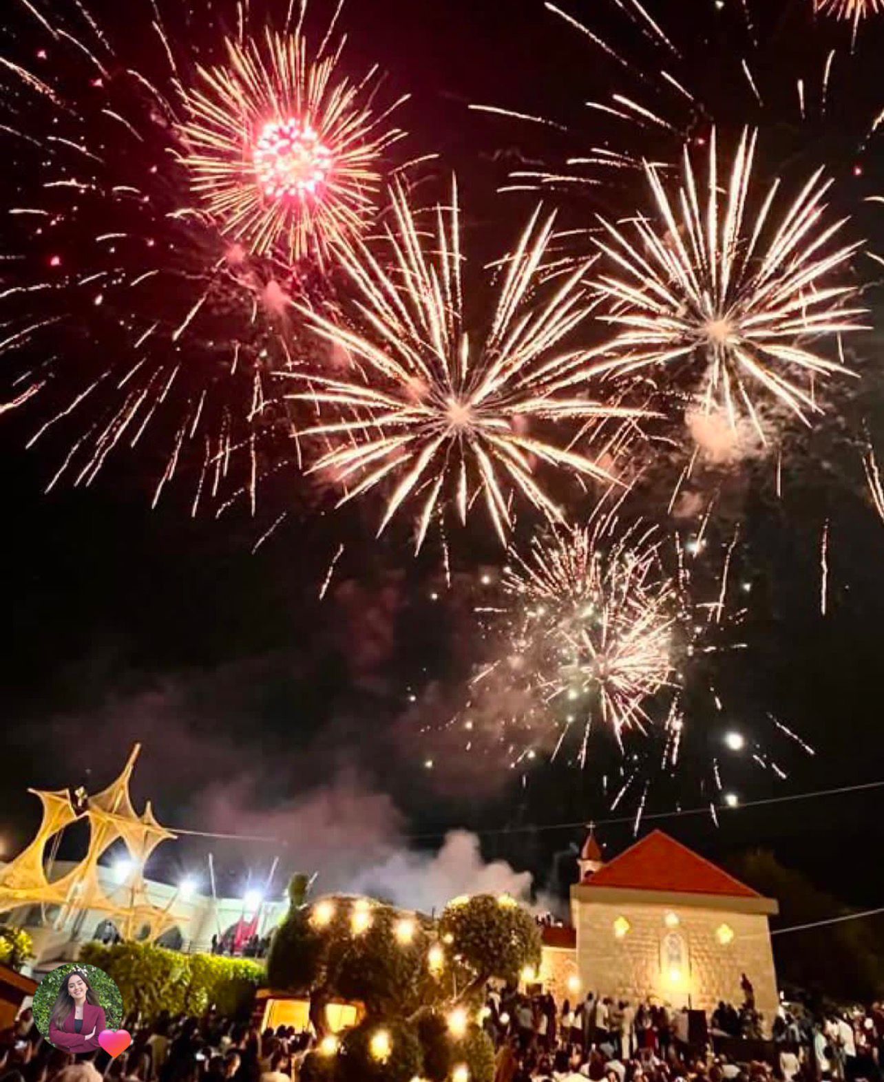 Fireworks exploding above a church and crowd during a nighttime festival event in Kobayat.
