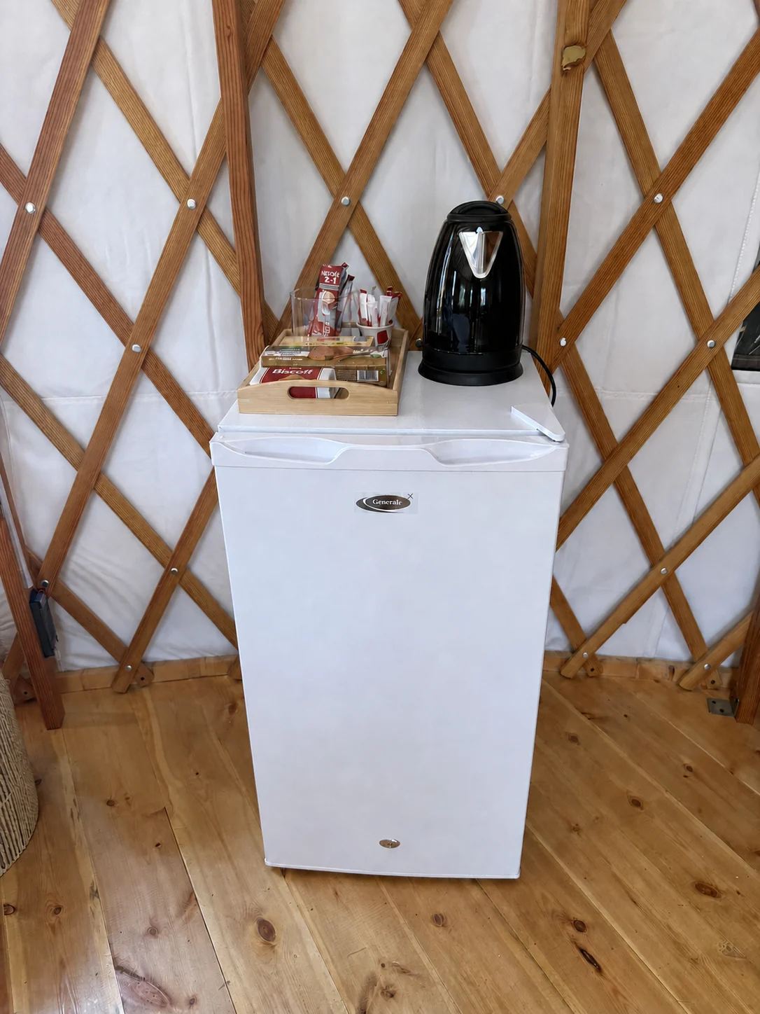 The yurt kitchenette: a small fridge with a kettle and tea tray against the lattice wall