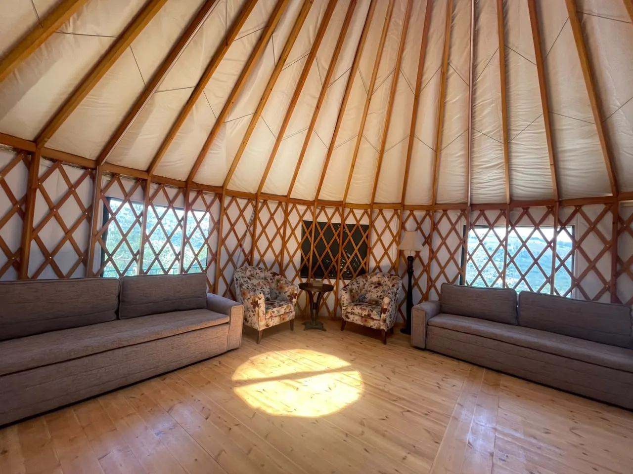 Inside a Premium Yurt: two sofas under the windows with sunlight from the skylight on the wooden floor