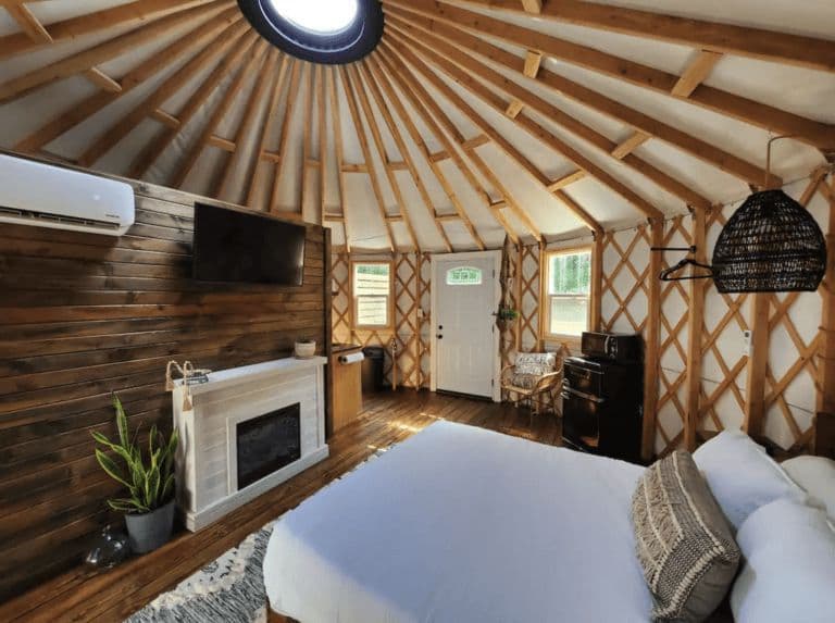 Modern yurt bedroom with wooden beams, fireplace, and cozy decor at Horizon Pines glamping site