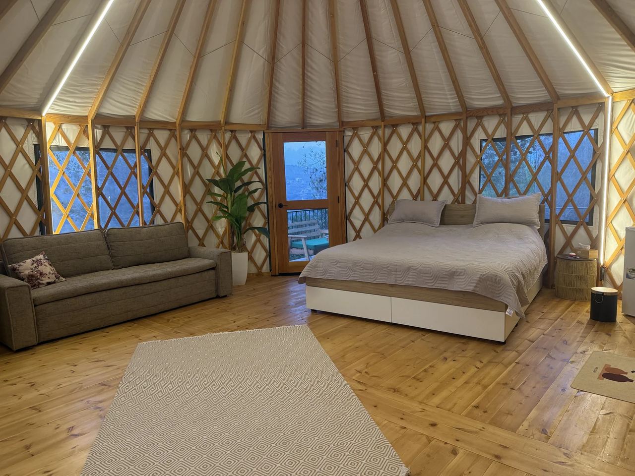 A Premium Yurt in the evening, with warm LED lighting along the roof beams over the bed and sofa