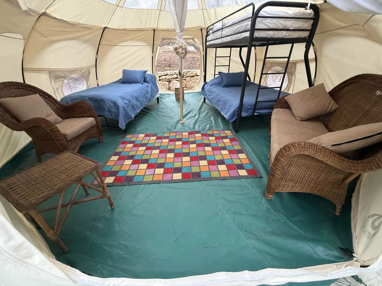Inside a Lotus Belle tent with a bunk bed, single beds and wicker chairs