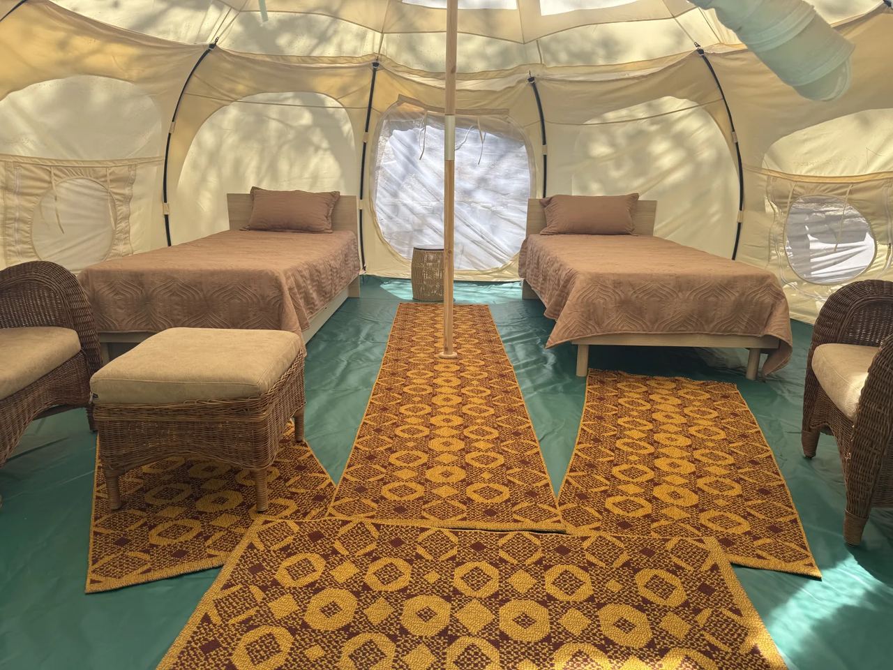Inside a Lotus Belle tent: single beds, wicker chairs and a patterned rug under the canvas