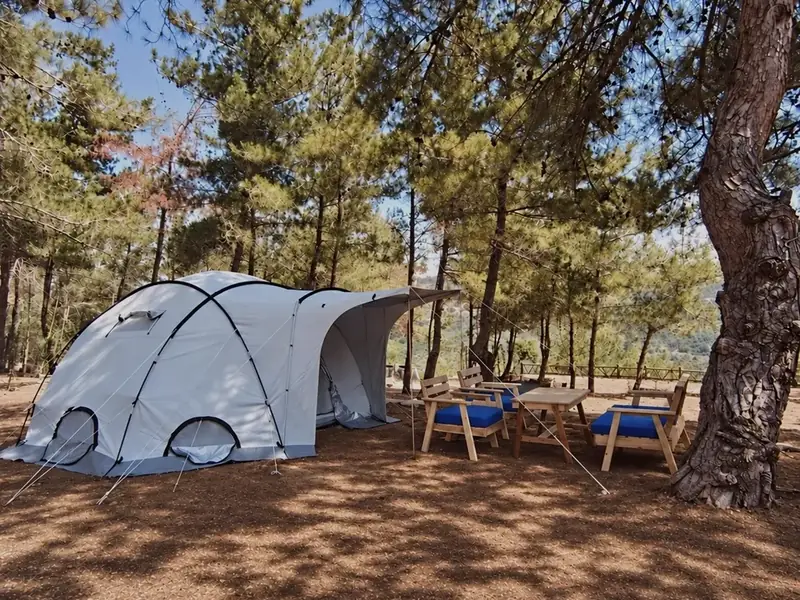 Dome tent with its awning open beside a wooden table and cushioned chairs at the Horizon Pines family camping area, Kobayat, Lebanon