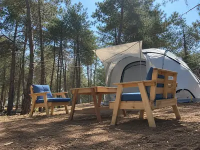 Wooden armchairs and a table in the shade, with a dome tent and open awning behind