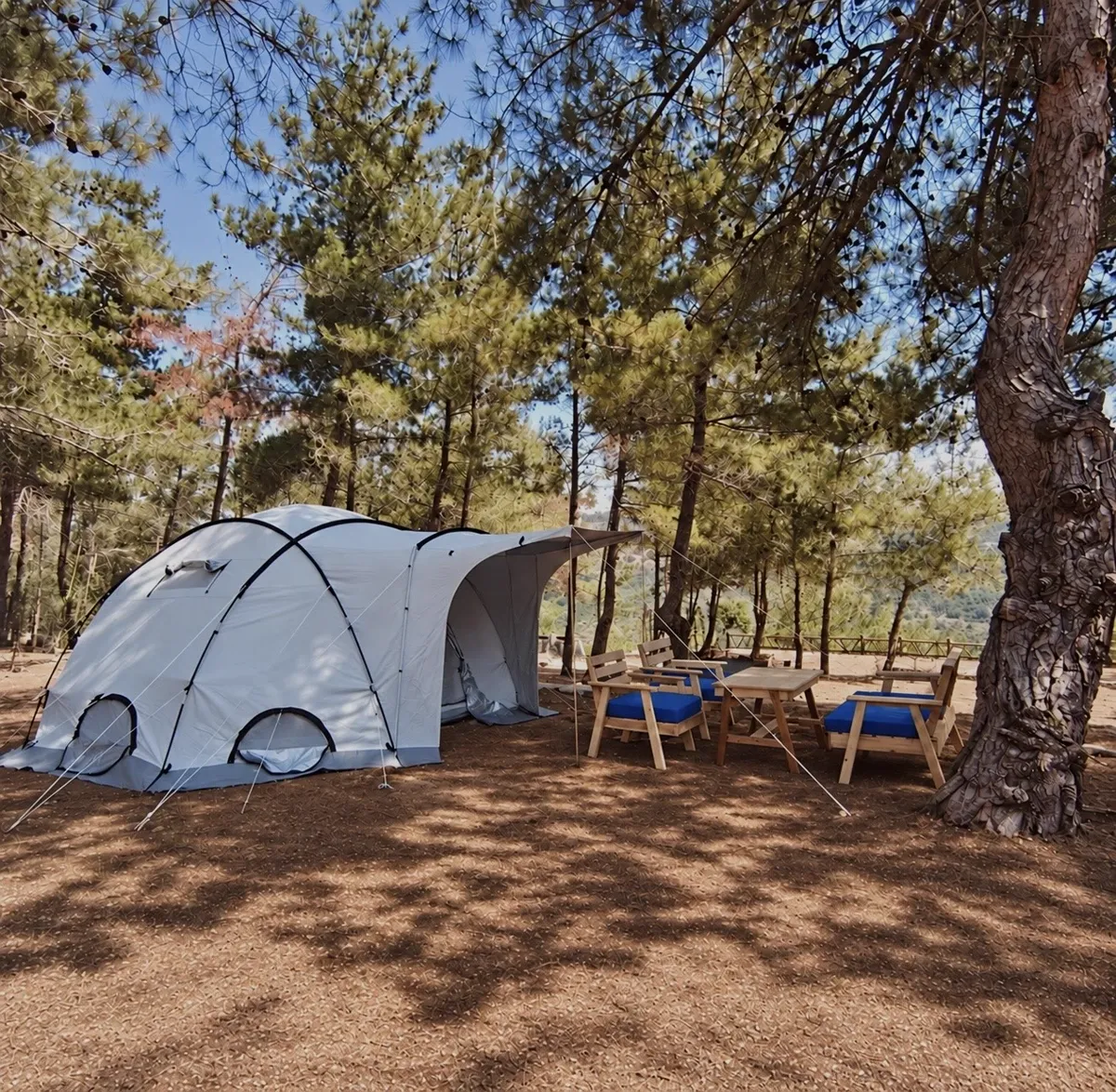Dome tent with its awning open beside a wooden table and cushioned chairs at the Horizon Pines family camping area, Kobayat