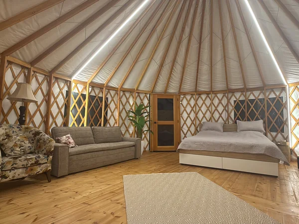 The whole yurt from the door: sofa bed, double bed, rug and fridge under the domed roof
